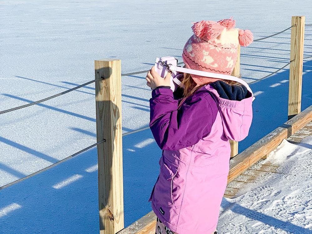 A young girl holds a camera up to her face on a snowy day. Taking pictures is one tip for how to travel with kids.