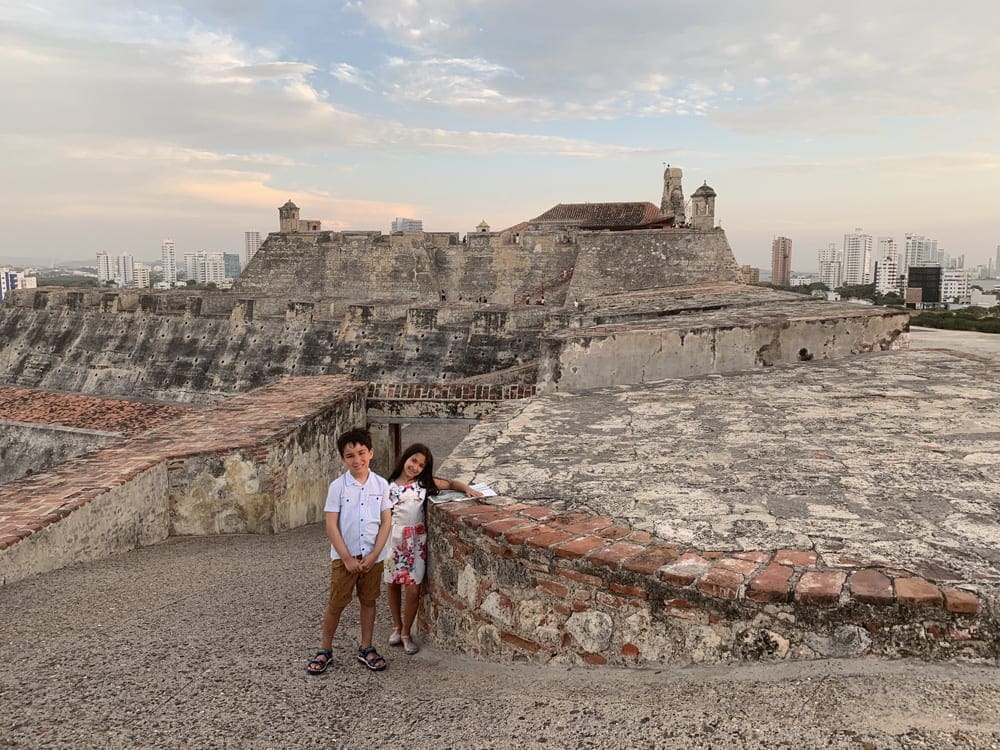 Two kids stand atop the the Castillo San Felipe Fortress at sunset, one of the best things to do on this Cartagena itinerary for families.