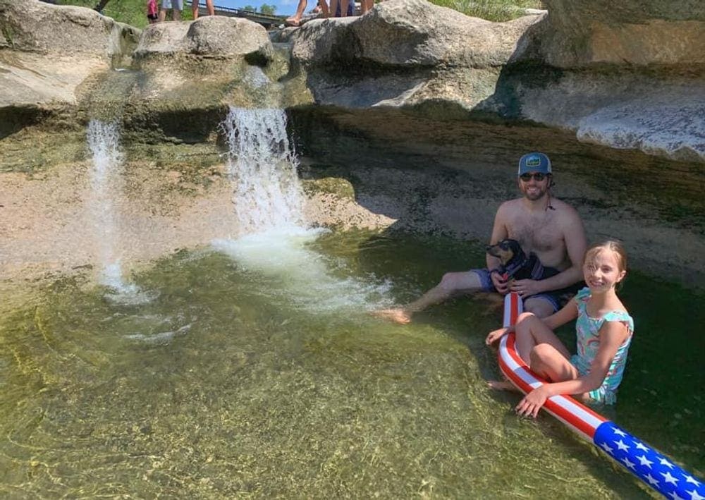 A dad and his daughter sit in the water at Bull Creek near Austin.