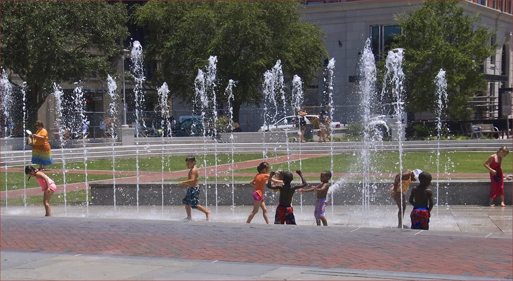 Kids splash and play in the Ellis Square Fountains on a sunny day.