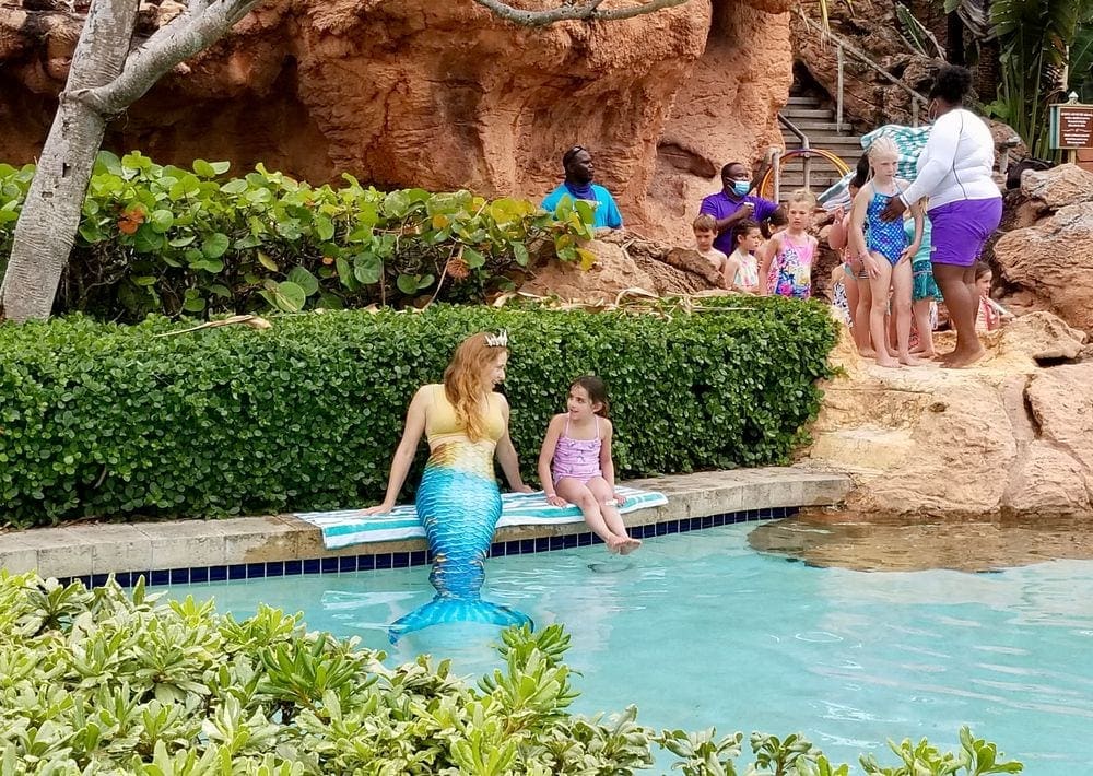 A young girl talks to a mermaid at a pool in Atlantis Bahamas while other kids wait their turn.