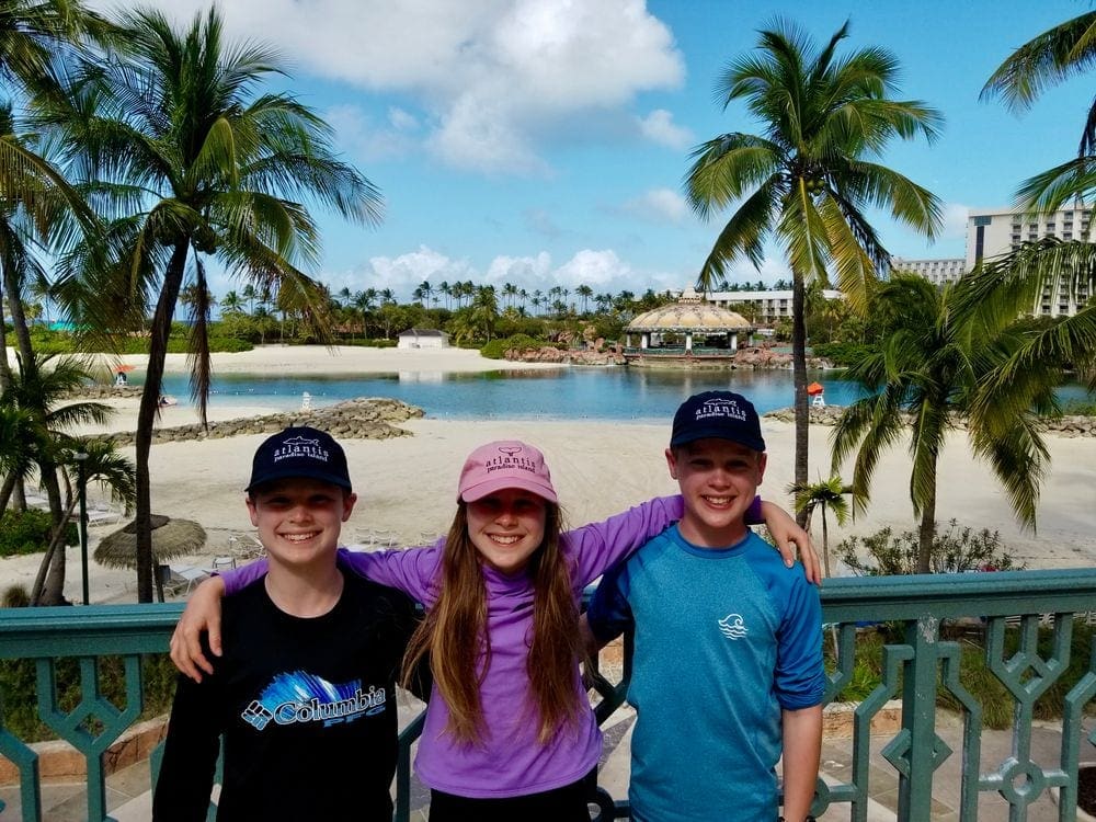Three kids stand togehter smiling on a sunny day in the Bahamas.