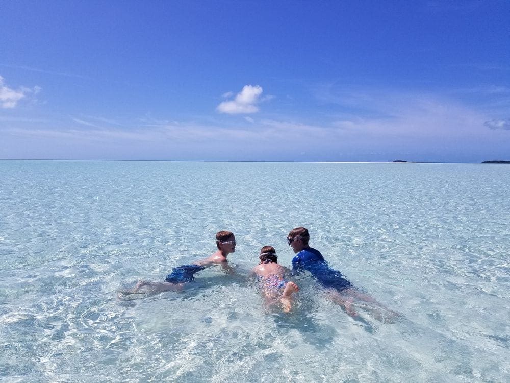 Two boys and a girl snorkeling for sand dollars in the clear blue water of the Bahamas.