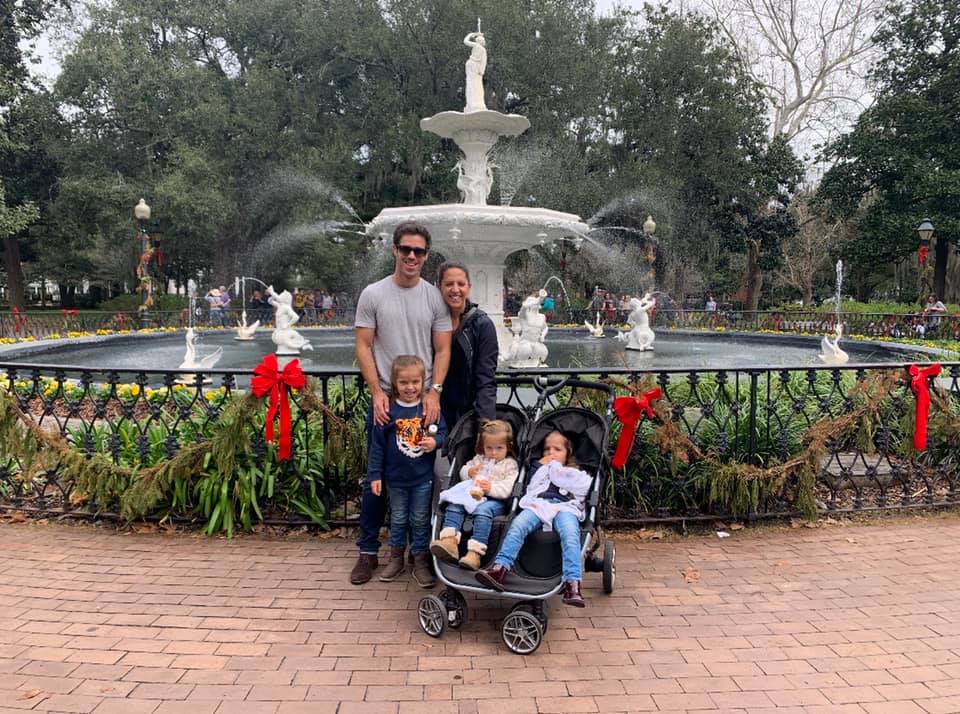 A family stands around a charming fountain in Savannah, decked out for the holiday season with a green and red garland.