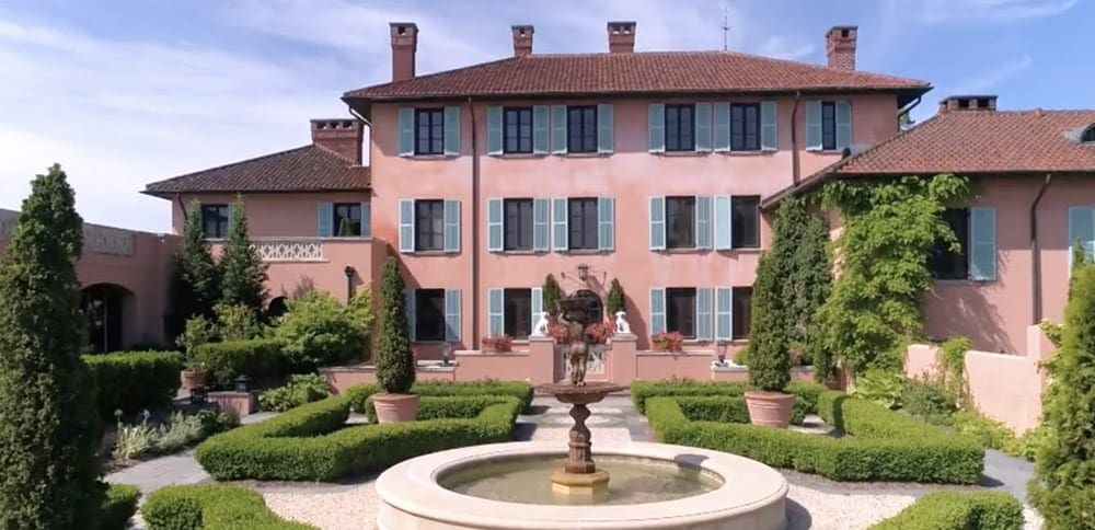 The pink buildings of Glenmere Mansion, with lush gardens in front of the main entrance, as well as a fountain.
