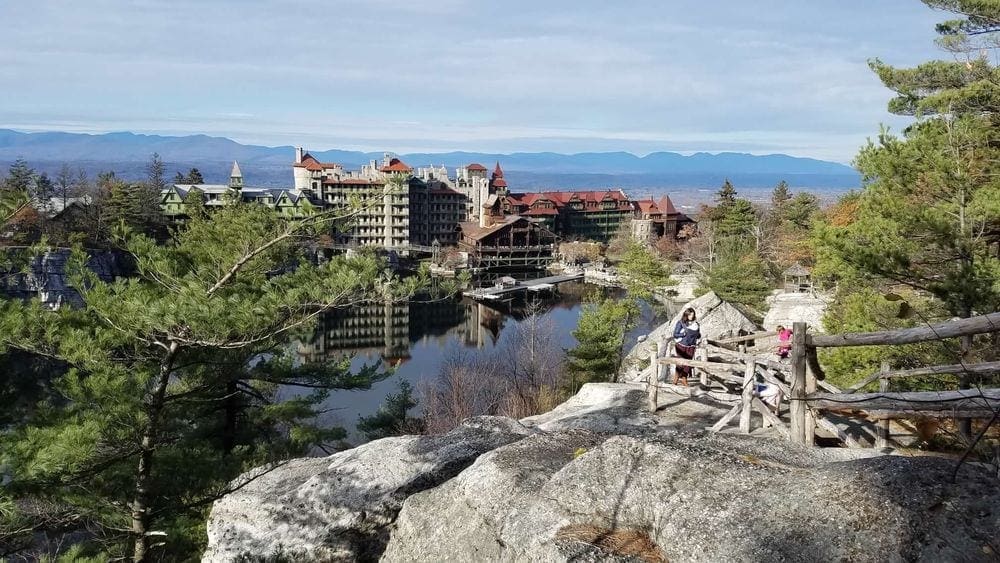 A view of Mohonk Mountain House, one of the best summer lake resorts in the Northeast for families, across the water, with a view of a walking trail.
