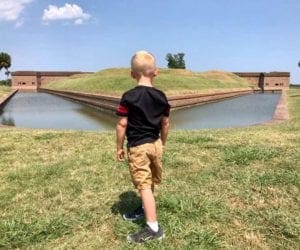 A young boy explores Old Fort Jackson on a sunny day while looking at the moat around the buildings.