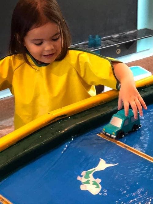 A young girl moves a car along a water table at the Charleston Children's Museum.