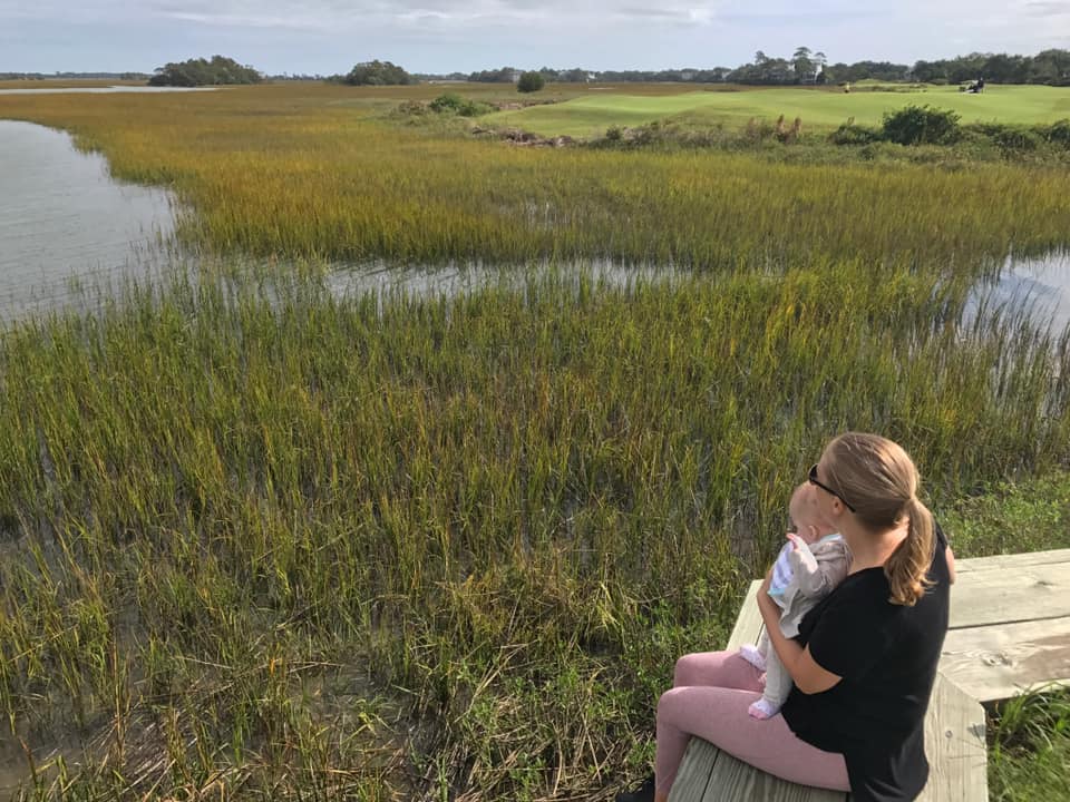 A mom holds her infant while sitting on a dock overlooking a marshy area near Charleston.