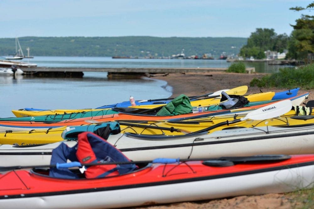 A series of colorful kayak rest on a beach on Madeline Island, a great stop for a Midwest road trip with kids.