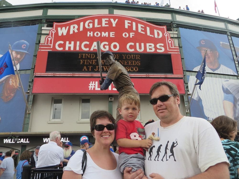 A family of three stands in front of the iconic Wrigley Field sign in Chicago.