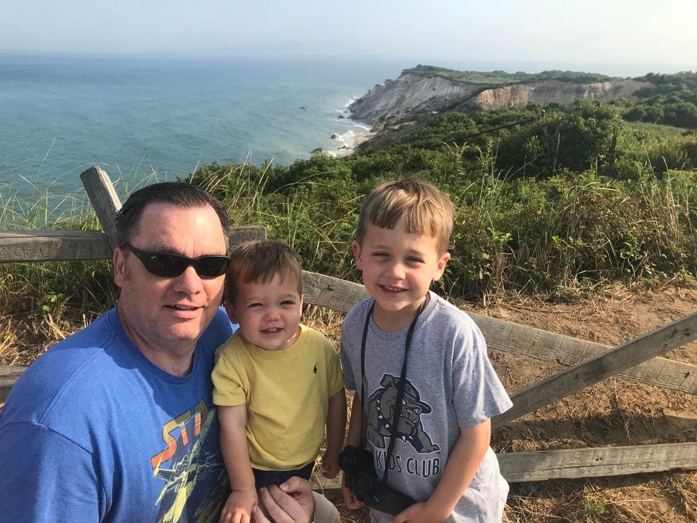 A dad and his two sons pose with the Aquinnah Cliffs behind them, one of the best things to do on your Family Vacation in Martha's Vineyard.