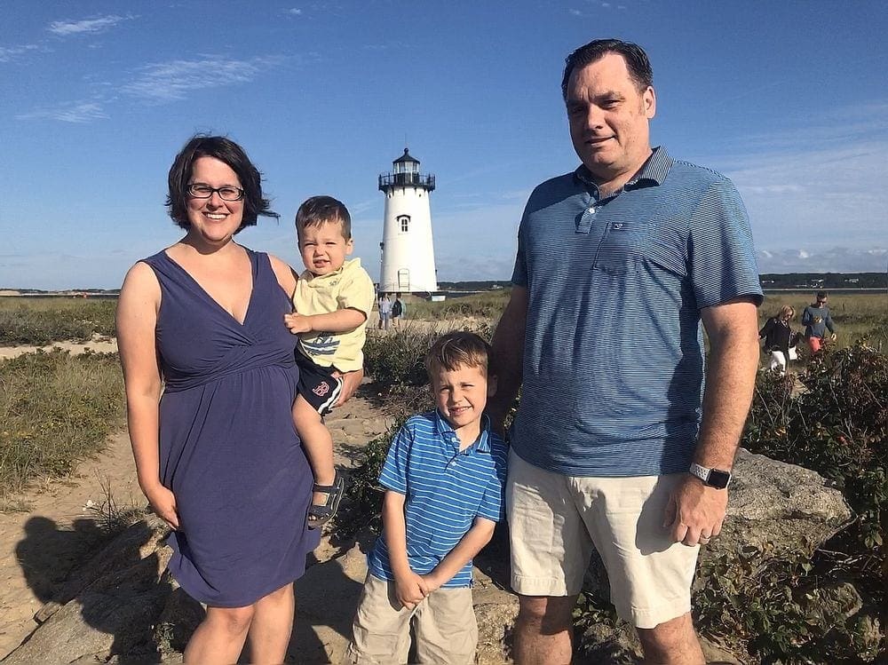 A family of four stands together smiling with the Edgartown Lighthouse in the background.