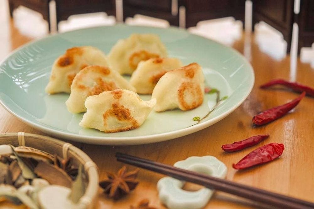 A blue plate holds a plate of dumplings with spices around the plate at Qing Xiang Yuan Dumplings.