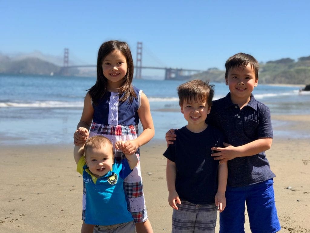 Four kids stand together while enjoy a beach day in the Bay Area.