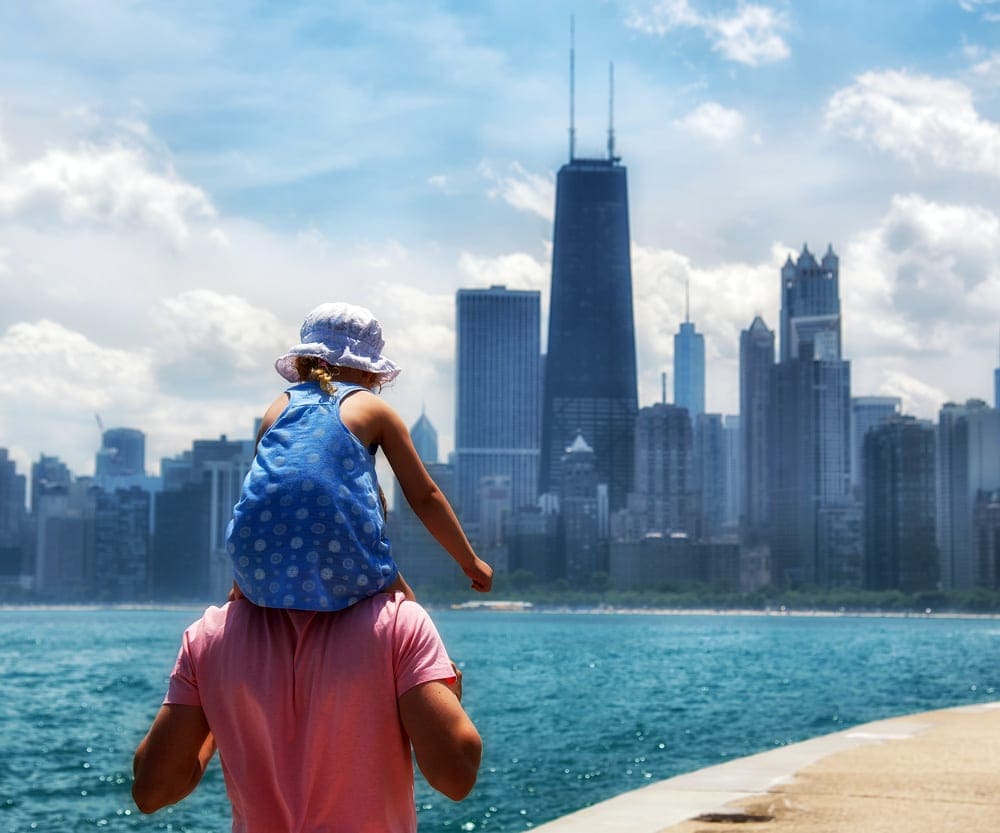 A young girl rides on her father's shoulders as the walk along the lakeshore with the skyline of Chicago in the distance, one of the best places in Northern Illinois for families.