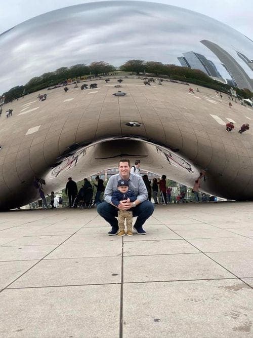 A dad crouches with his toddler son in front of "the Bean" in Chicago.