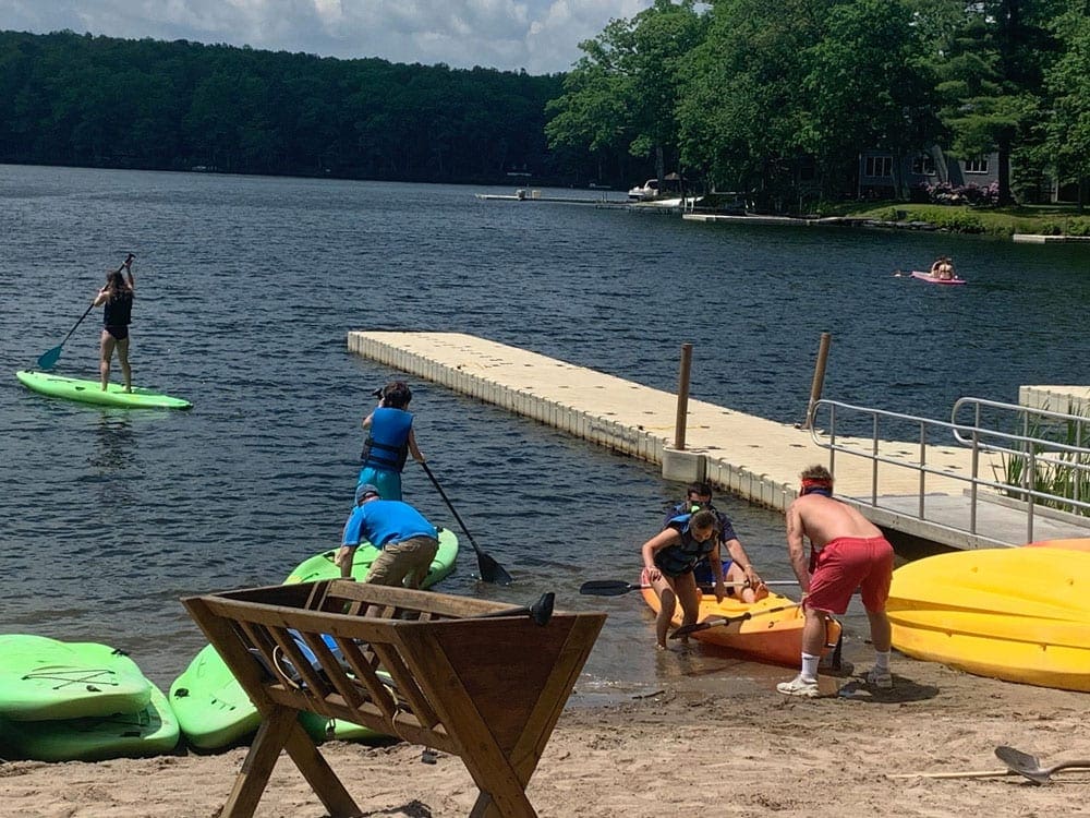 Kayakers enjoy the beach and water at the Woodloch Resort, one of the best summer lake resorts in the Northeast for families.