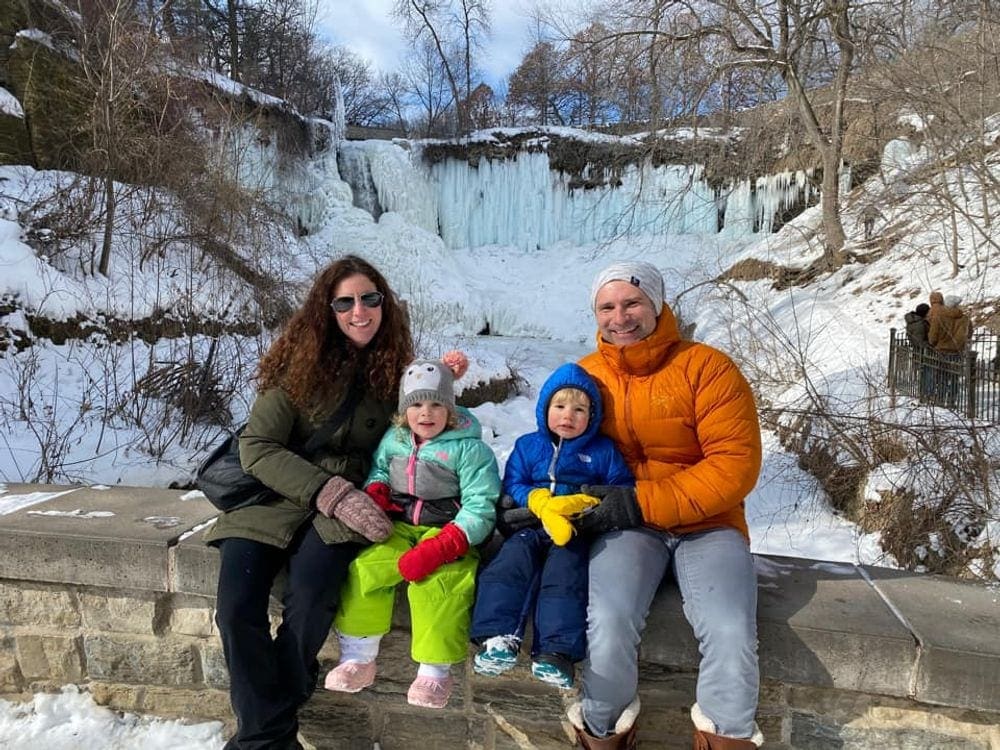 A family of four sits on a bridge with an icy Minnehaha Falls behind them.