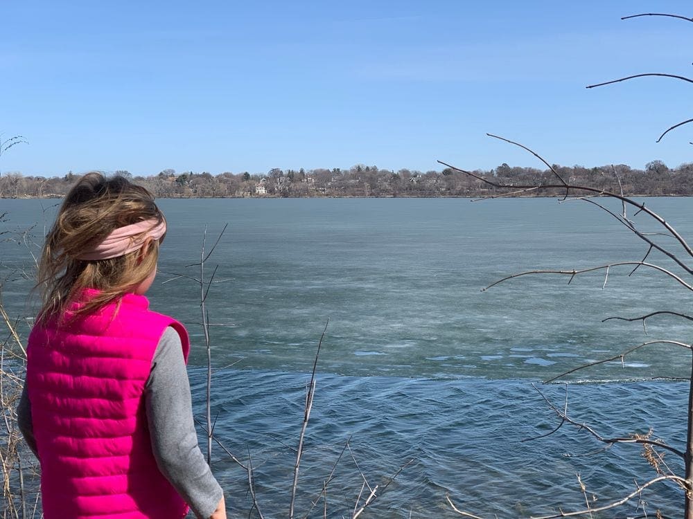 A young girl wearing a bright pink vests looks across Lake Harriet, one of the best free things to do in Minneapolis.