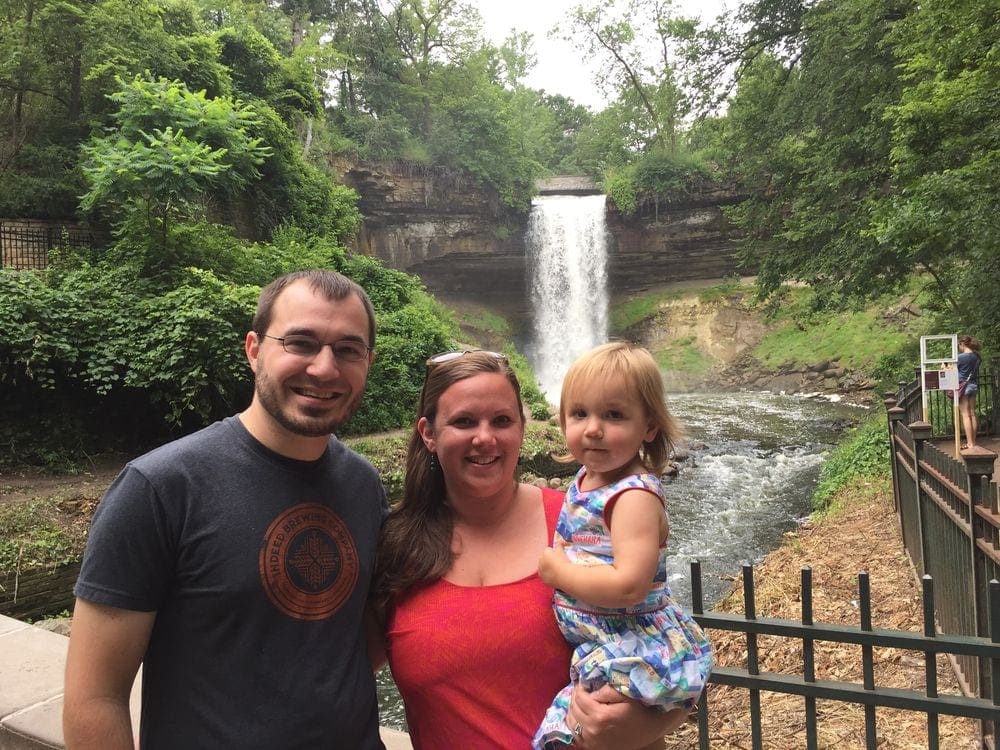 A family of three poses smiling with Minnehaha Falls behind them.