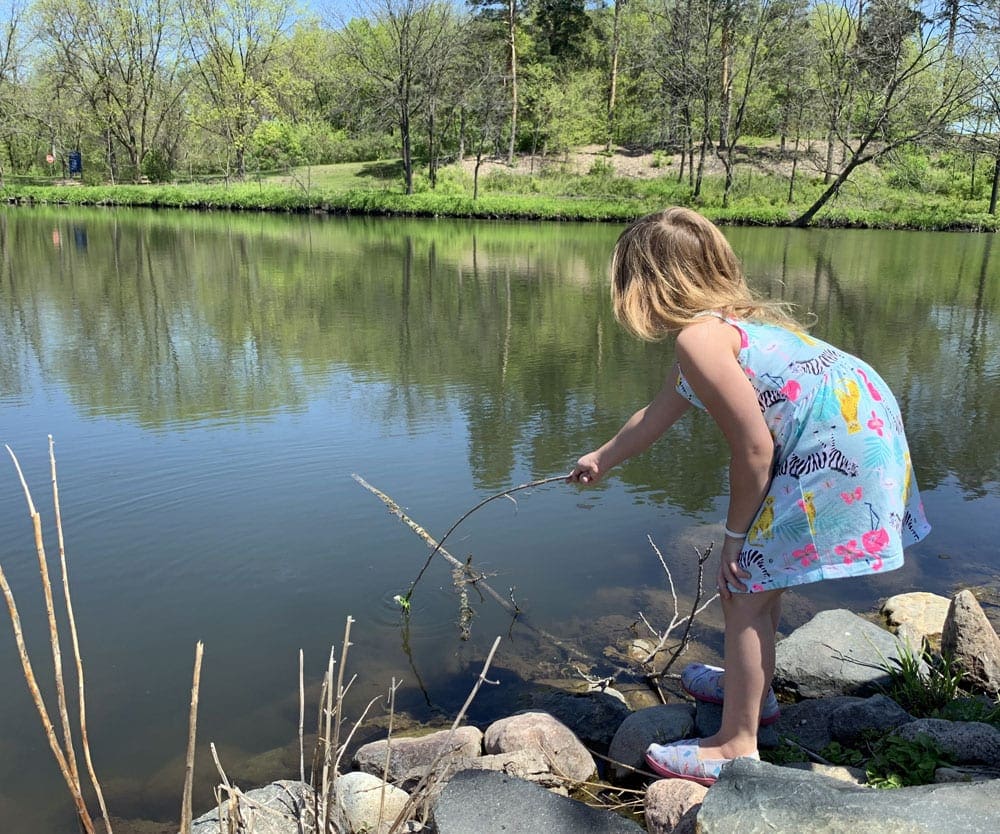 A young girl pokes a stick in the water on a sunny day in Northfield, Minnesota, one of the best weekend getaways from Minneapolis for families.