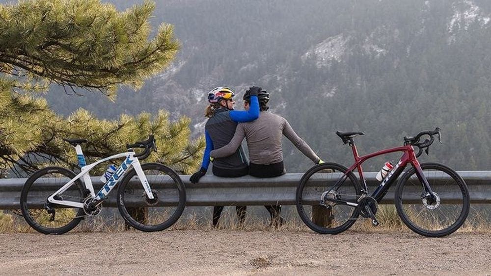 A couple sits together between their bicycles with a view of Acadia National Park in the distance.