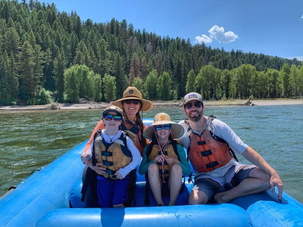 A family of four smiles while rafting down the Snake River, one of the best things to do in Grand Tetons National Park with kids.