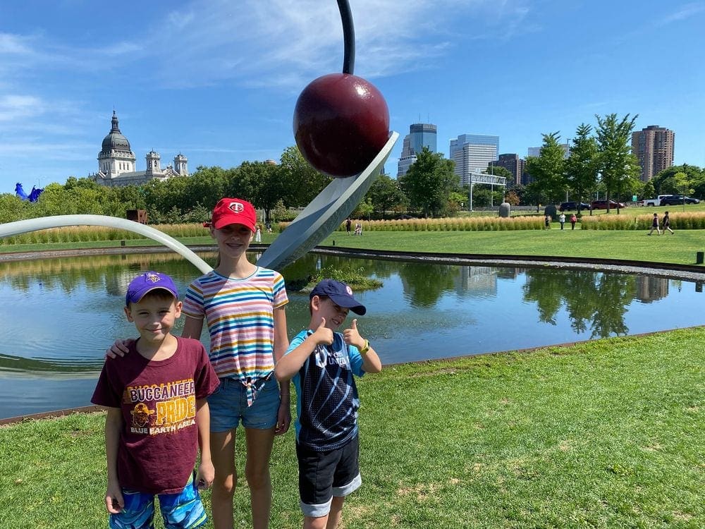 Three kids stand in front of the Spoon and Cherry art installation in Minneapolis.