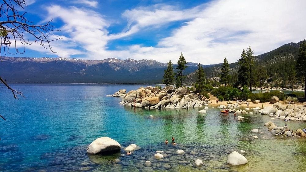 Several people swim and explore the rocks on the shore of Lake Tahoe.