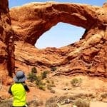 A young boy wearing a yellow shirt and a blue sun hat looks at the iconic Utah arches at Arches National Park, one of the best things to do in Moab with kids.
