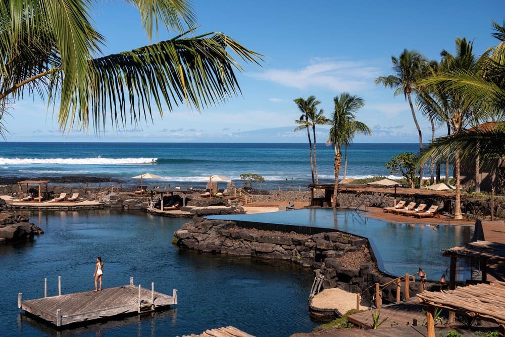 A series of pools at the Four Seasons Resort Maui at Wailea, with pool-side seating and many nearby palm trees.