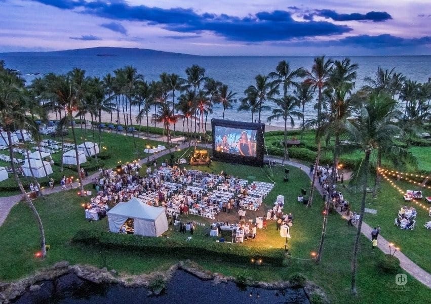 An aerial view of guests watching an outdoor movie near the ocean at Grand Wailea Maui, A Waldorf Astoria Resort, one of the best hotels in Hawaii for a family vacation.