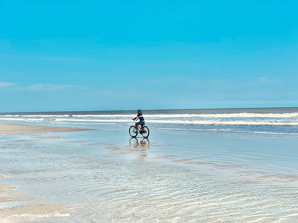 A young child bikes along the beach through sand and water on Kiawah Island.