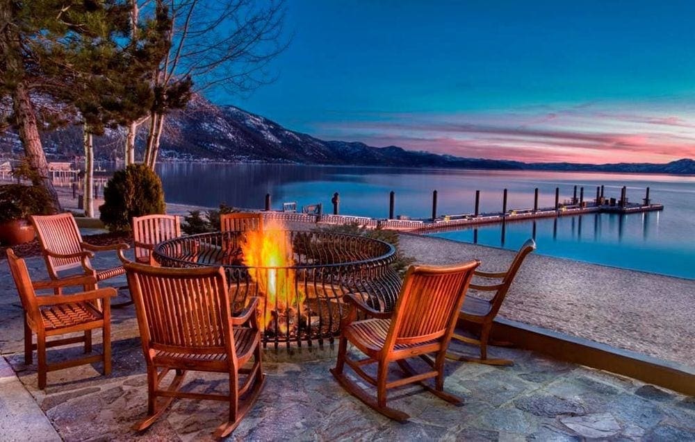 Several empty chairs surround a fire on a cool night in Lake Tahoe, nearby the lake and beach.