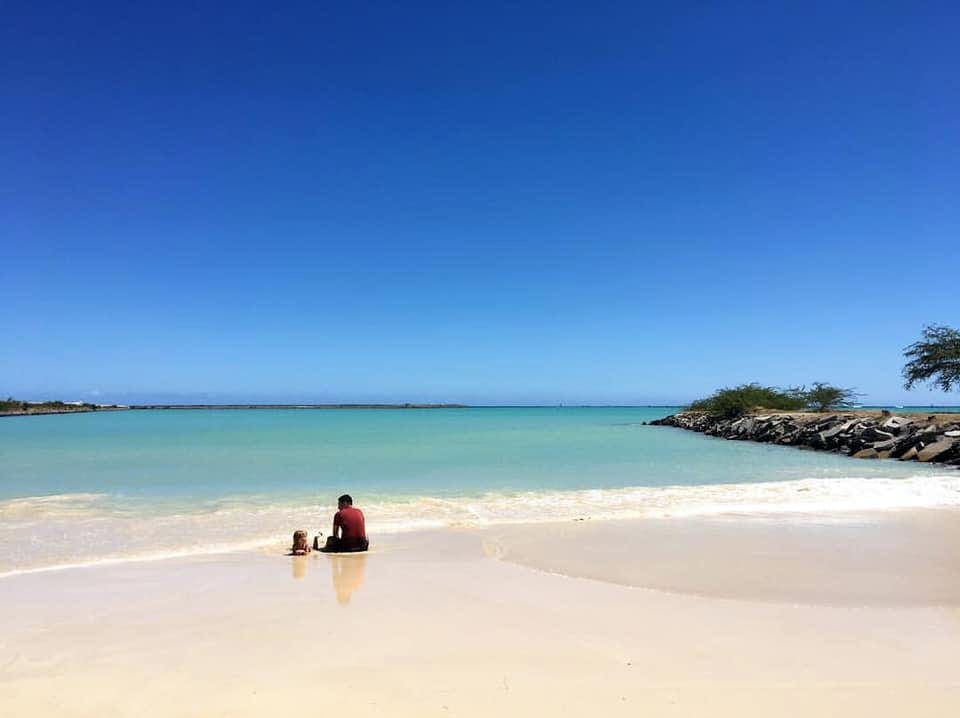 A young boy and his dad sit on a vast, empty beach in Oahu.
