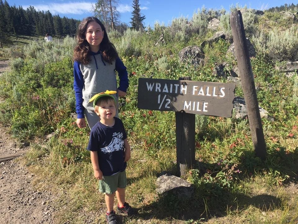 Two kids stand near a sign for Wraith Falls in Yellowstone National Park.