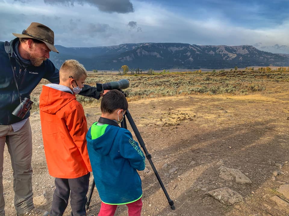 Two boys stand with their dad using a large lens to view bison along the Lamar Valley in Yellowstone National Park.