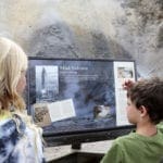 Two kids look at a sign inside Yellowstone National Park.