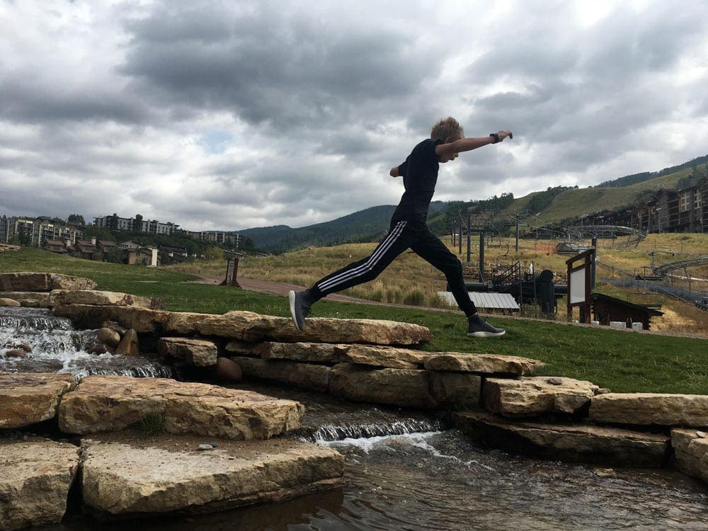 A pre-teen boy leaps across rocks while explore a local Colorado park.