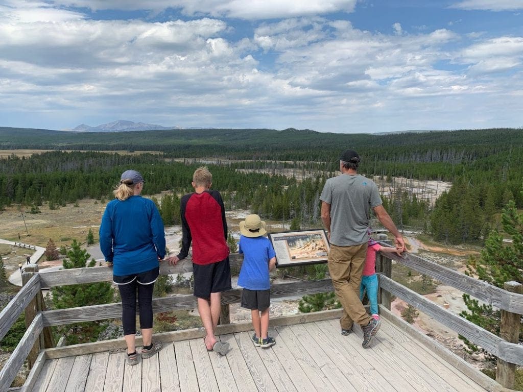 A family of five stands along a outlook looking out over a scenic view of Yellowstone National Park.