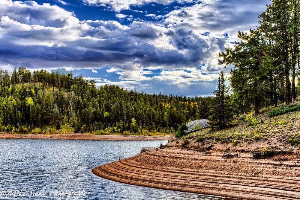 A stunning lakeshore, featuring evergreens on the distant shore and clear blue skies in Colorado.