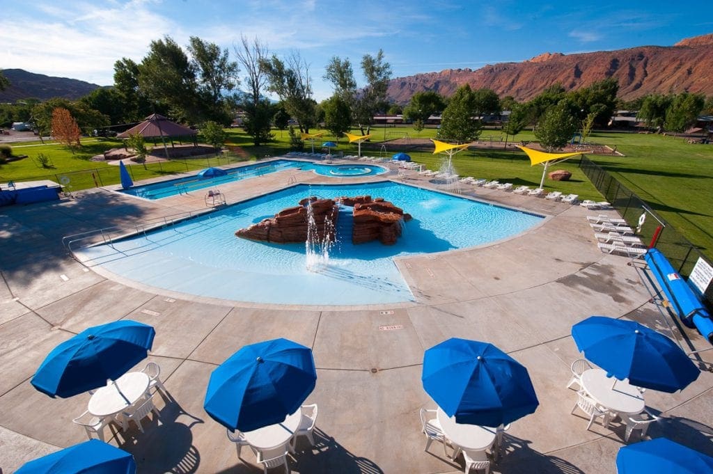 The pool at Moab Recreation & Aquatic Center, surrounded by blue umbrellas and lush grounds.