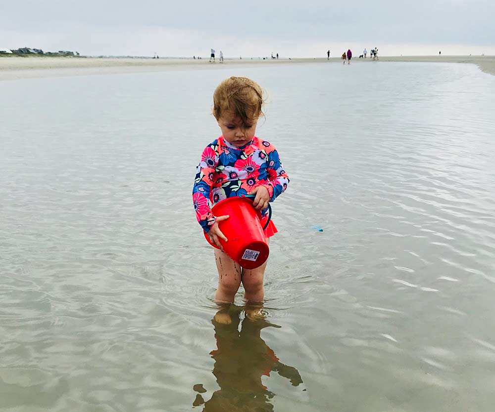 A young girl with a bright red sand pail plays off the shore from Sullivan Island, one of the best islands in South Carolina for families.