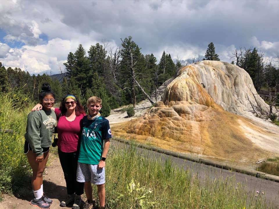 A mom and her two kids stand together while exploring Yellowstone National Park, featuring the Grand Mammoth Hot Springs.