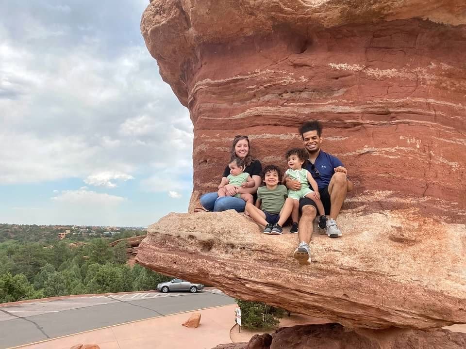 A family of five sits together smiling, tucked into a rock ledge while exploreing Garden of the Gods, one of the best things to do in Colorado Springs with kids.