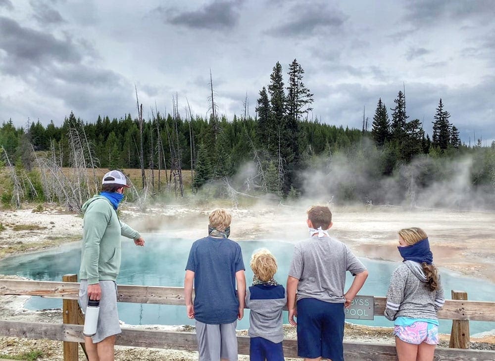 A family of five peers into the teal hot spring at Yellowstone National Park.
