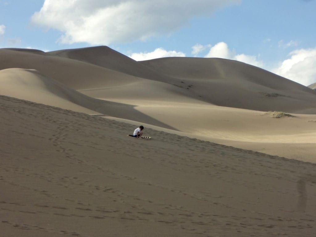 A lone boy sits in the sand while exploring the dunes of Great Sand Dunes National Park and Preserve in Colorado.