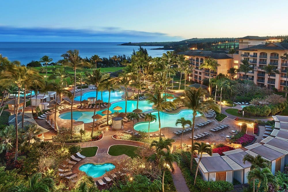 An aerial view of Sheraton Maui Resort & Spa at night, featuring well-lit paths, buildings, and pool area.