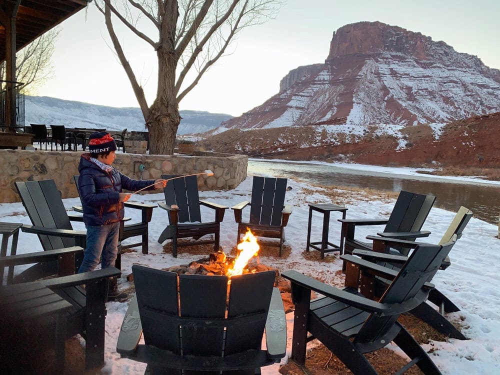 A young boy roasts a marshmallow over an outdoor fire while staying at Sorrel River Ranch Resort.